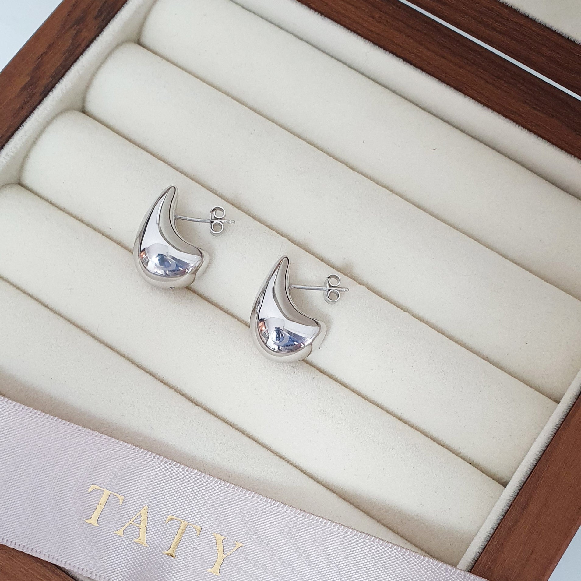 Boucles d'oreilles goutte en argent 925 rhodié posées sur un support à bijoux