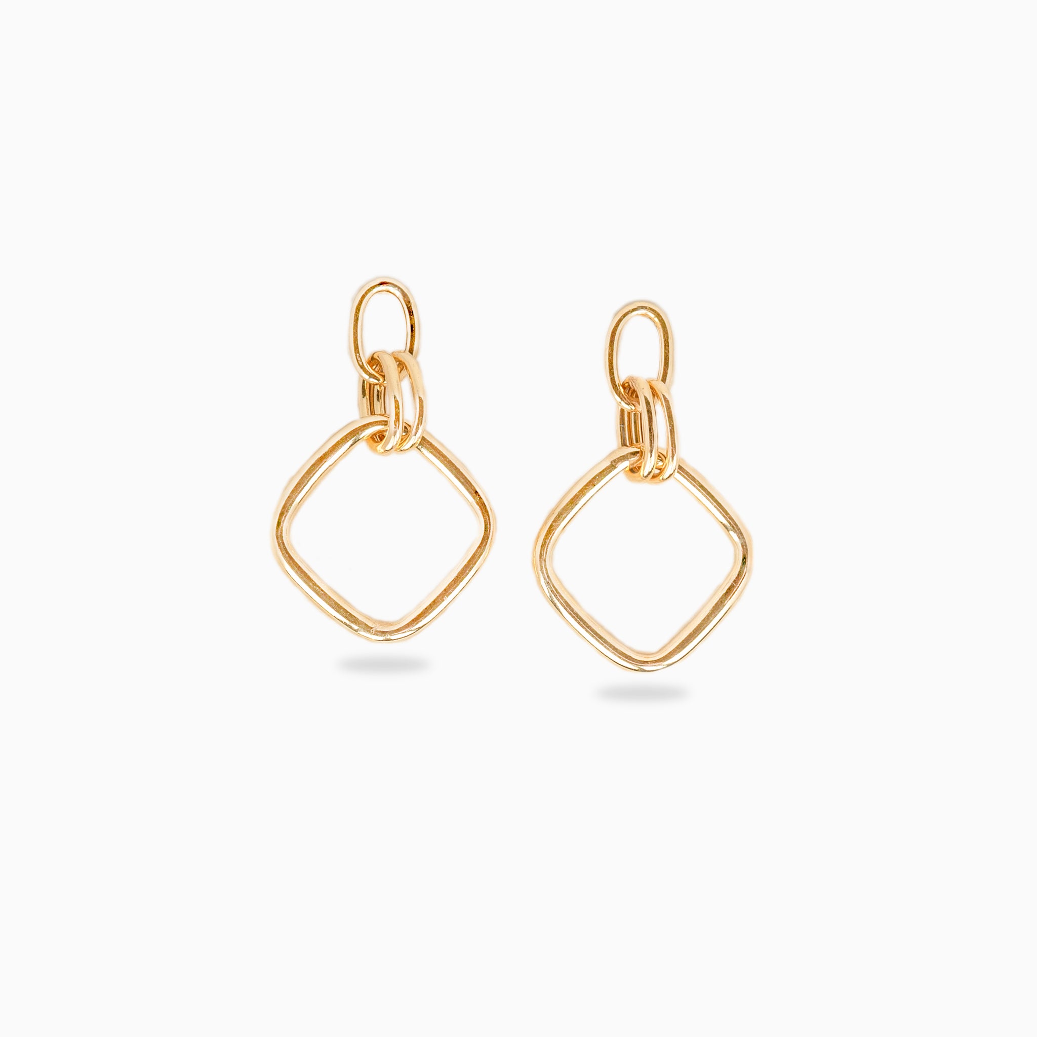 Boucles d'oreilles pendantes or de forme losange sur un fond blanc