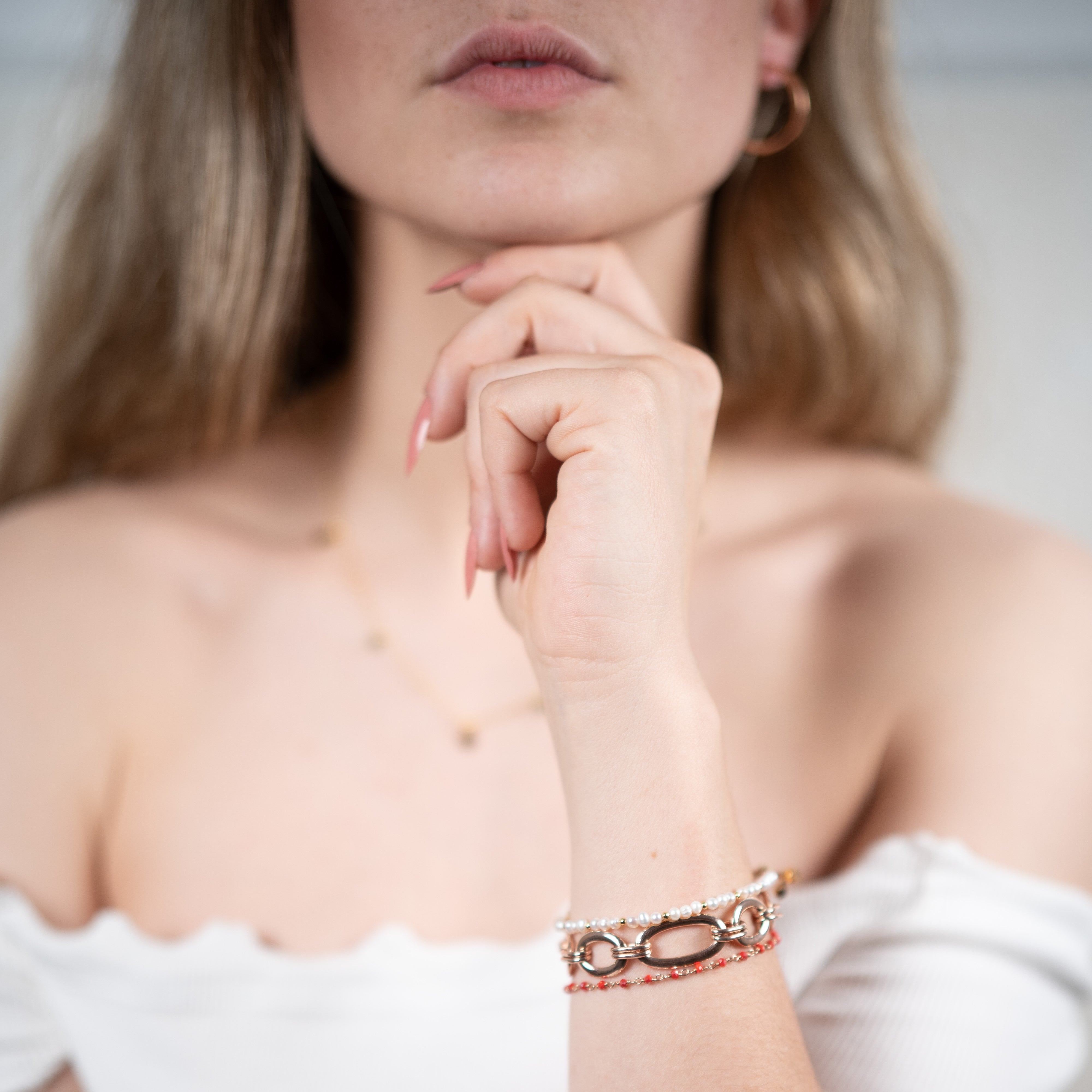 Drei Armbänder, darunter ein Naturperlenarmband aus Baumwolle, ein Karneolarmband und ein roségoldfarbenes Gliederarmband