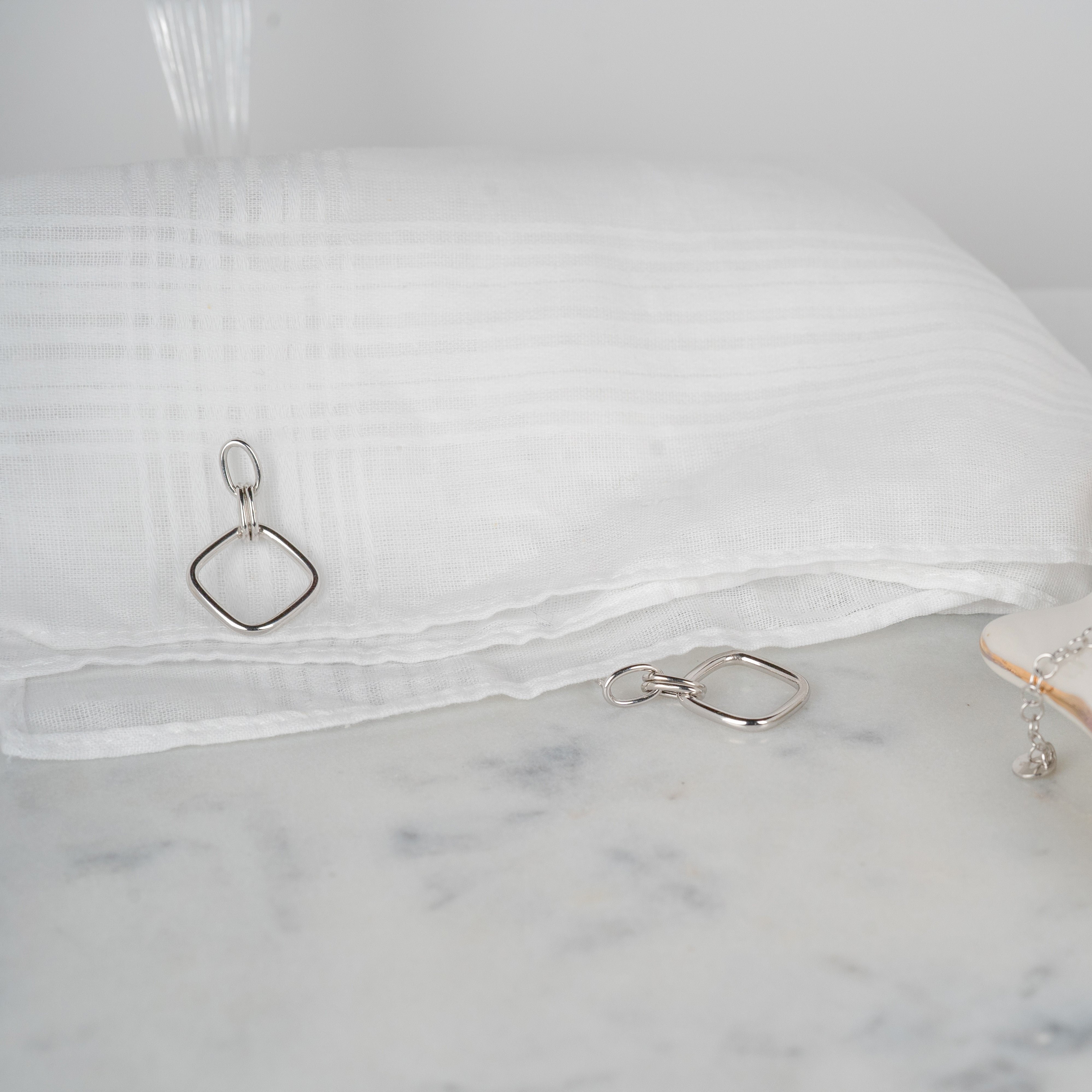 Boucles d'oreilles pendantes argent rhodié losange posées sur un tissu blanc