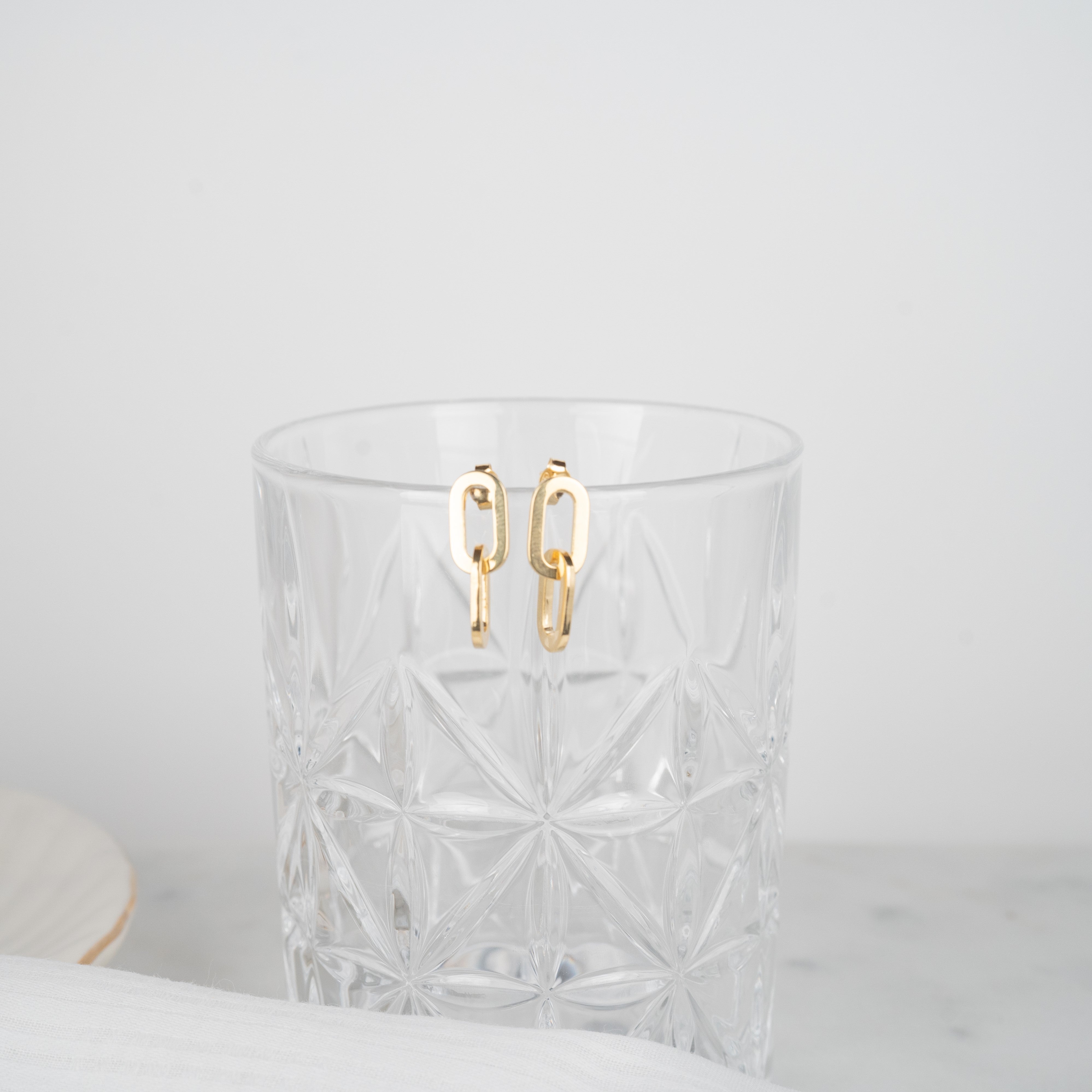 Ohrringe aus gelbgoldfarbenen Gliedern, die auf einem Glas sitzen