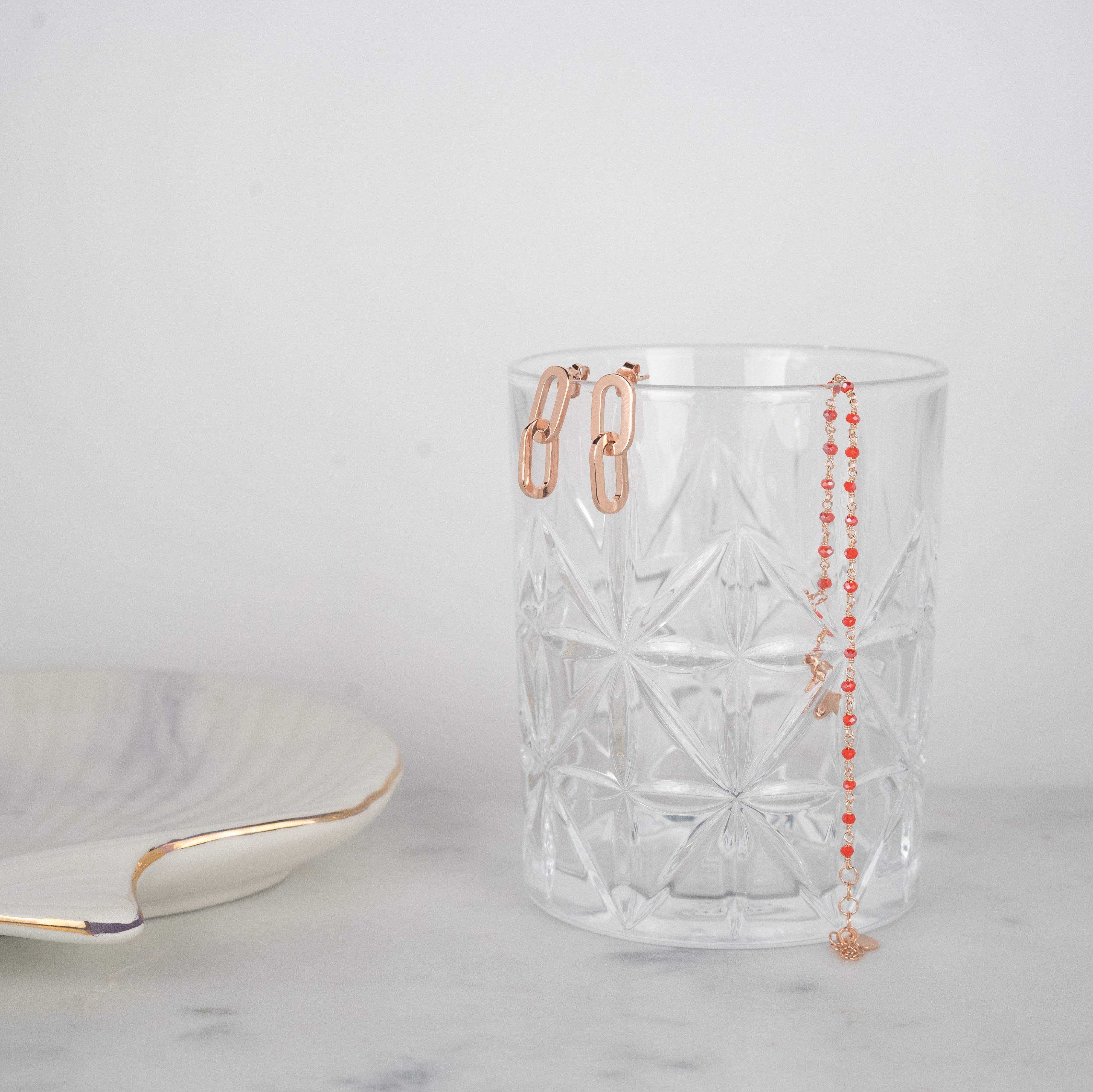 Link earrings and bracelet set on a glass next to a shell