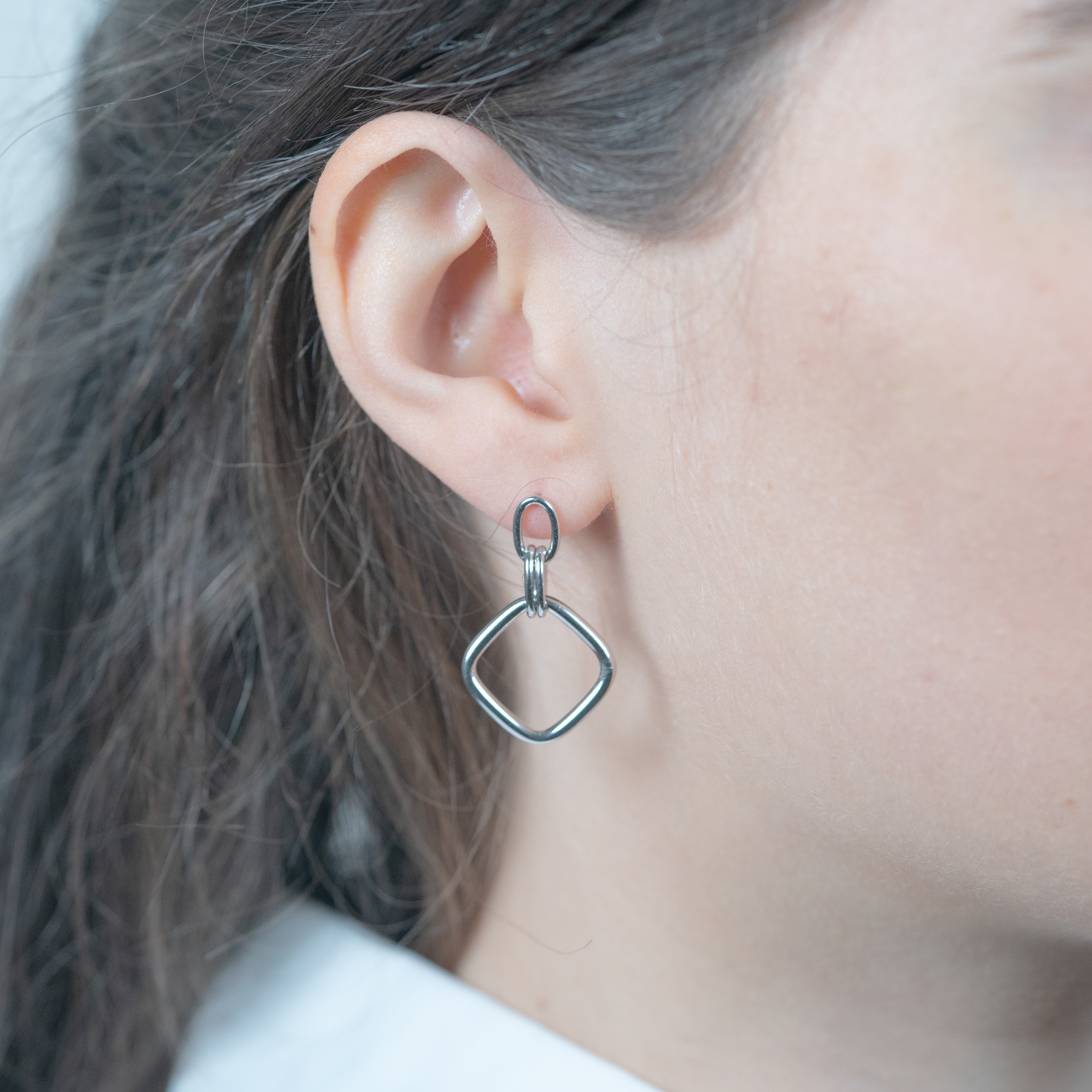 Rhodium-plated silver diamond-shaped dangling earrings worn on a model