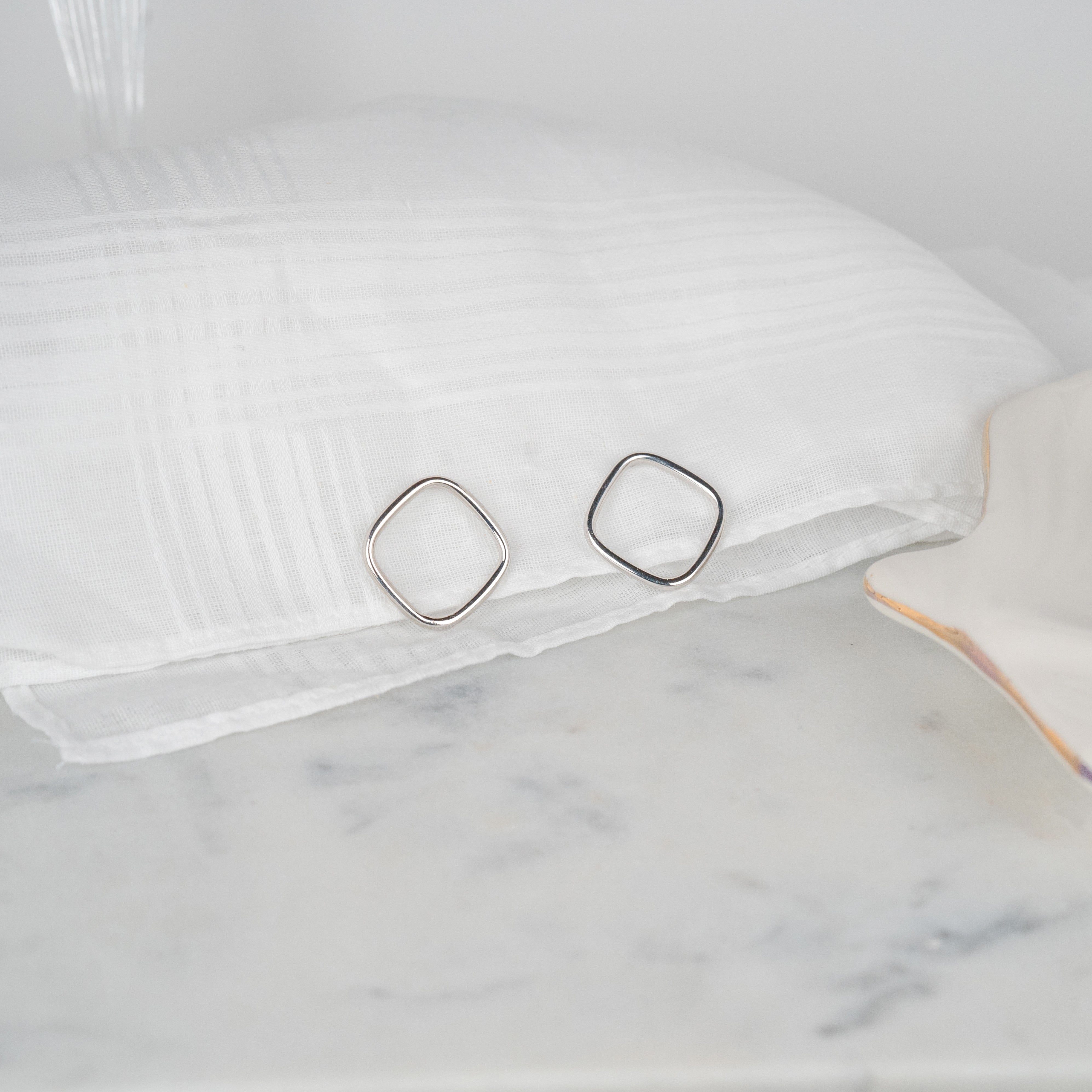 Boucles d'oreilles losanges couleur argent petit modèle posées sur un tissu blanc