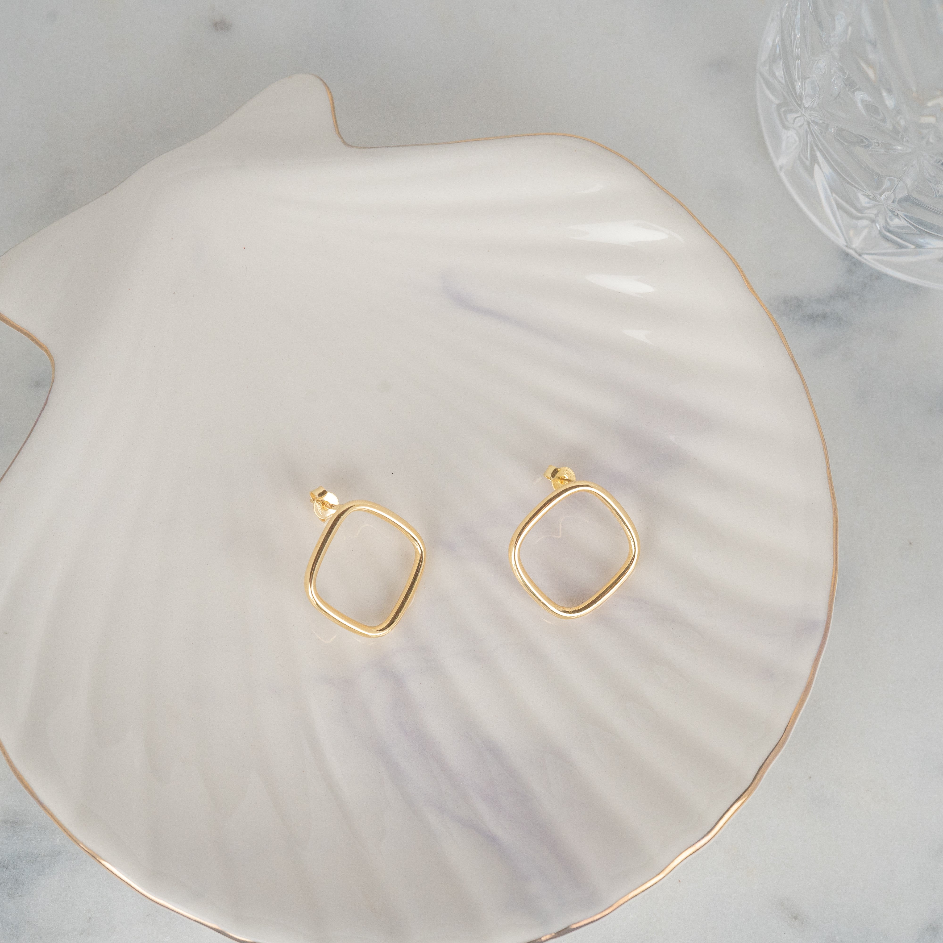 Boucles d'oreilles losanges or en argent 925 posées sur un coquillage