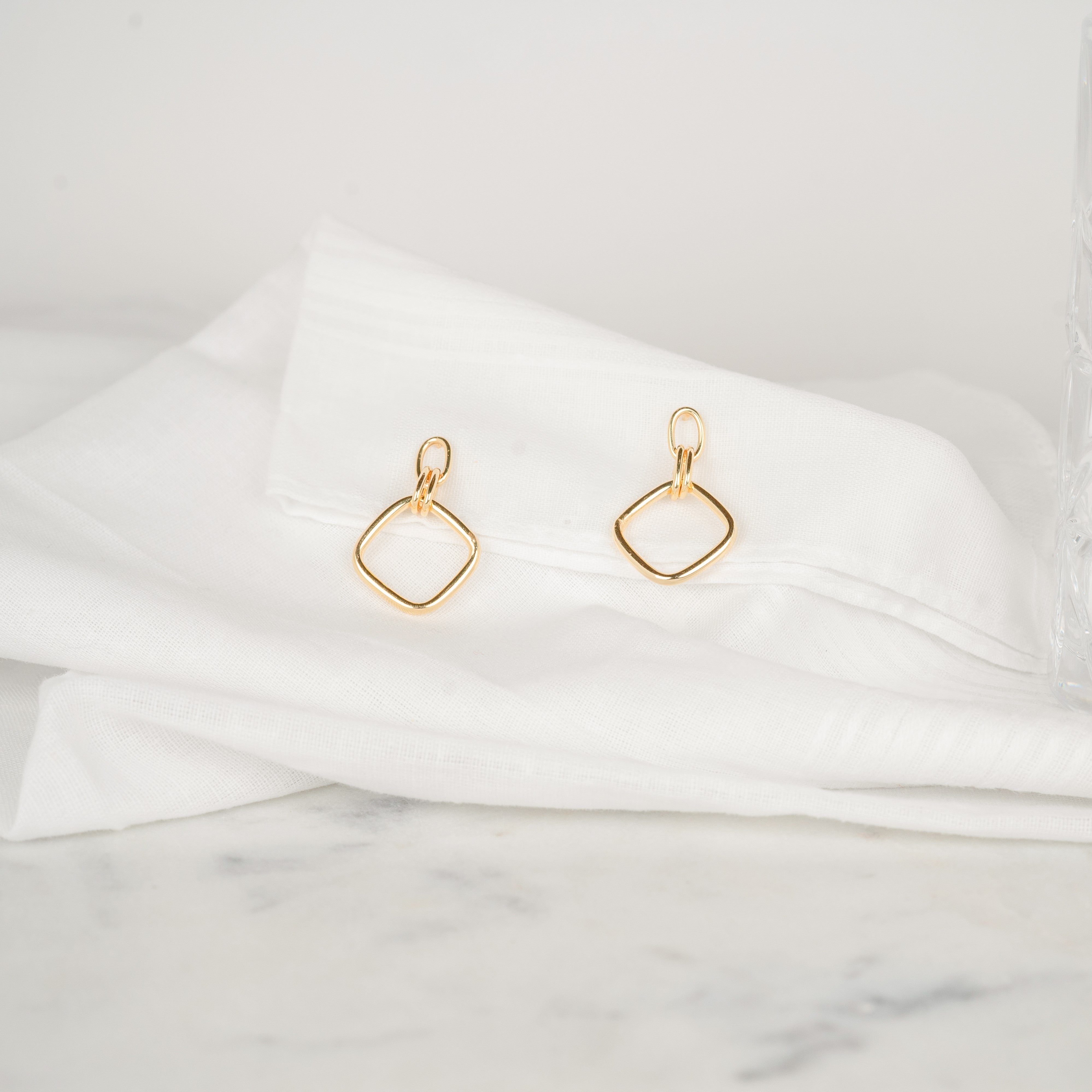 Boucles d'oreilles pendantes or losange en argent plaqué or jaune posées sur un tissu blanc