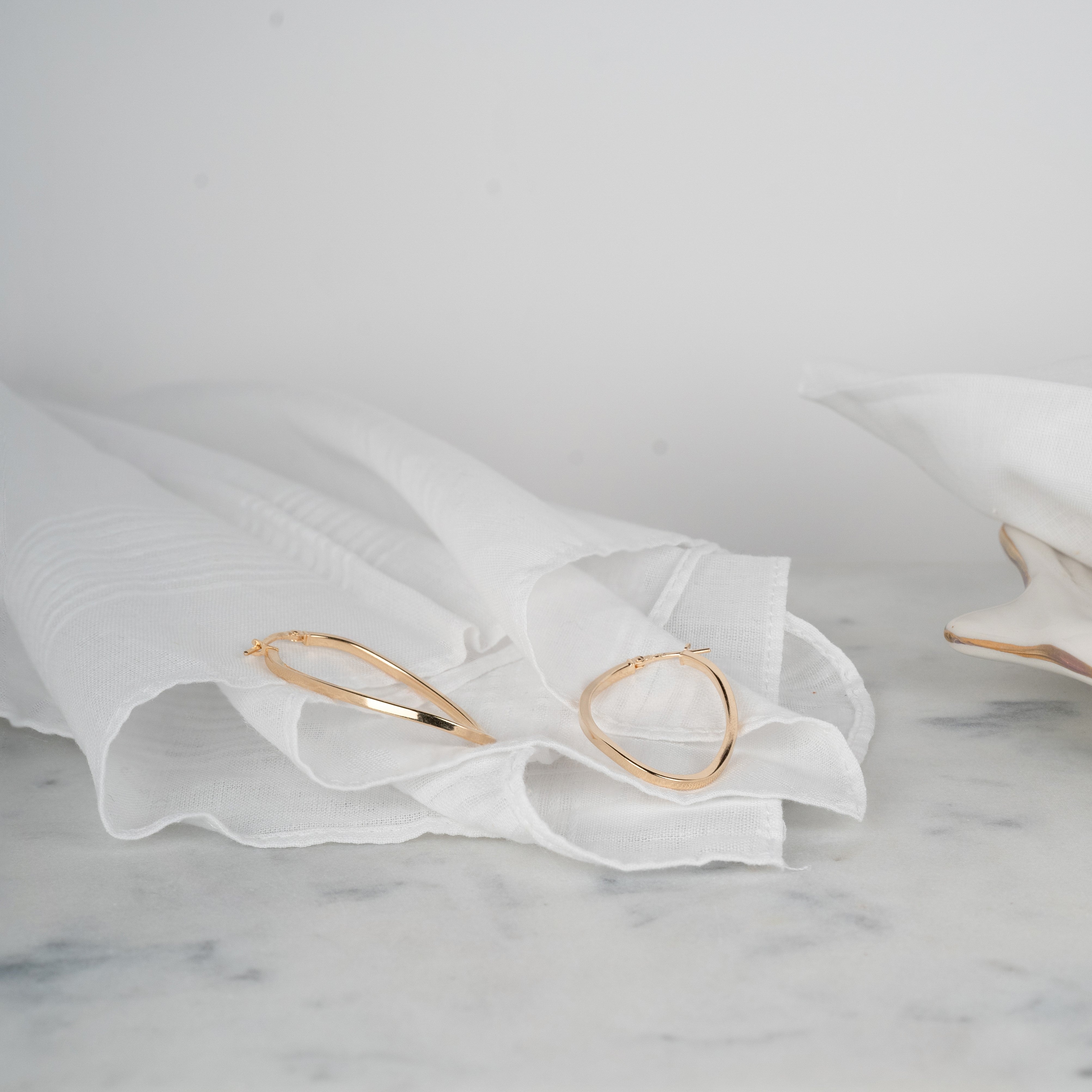 Yellow gold asymmetrical hoop earrings set on white fabric