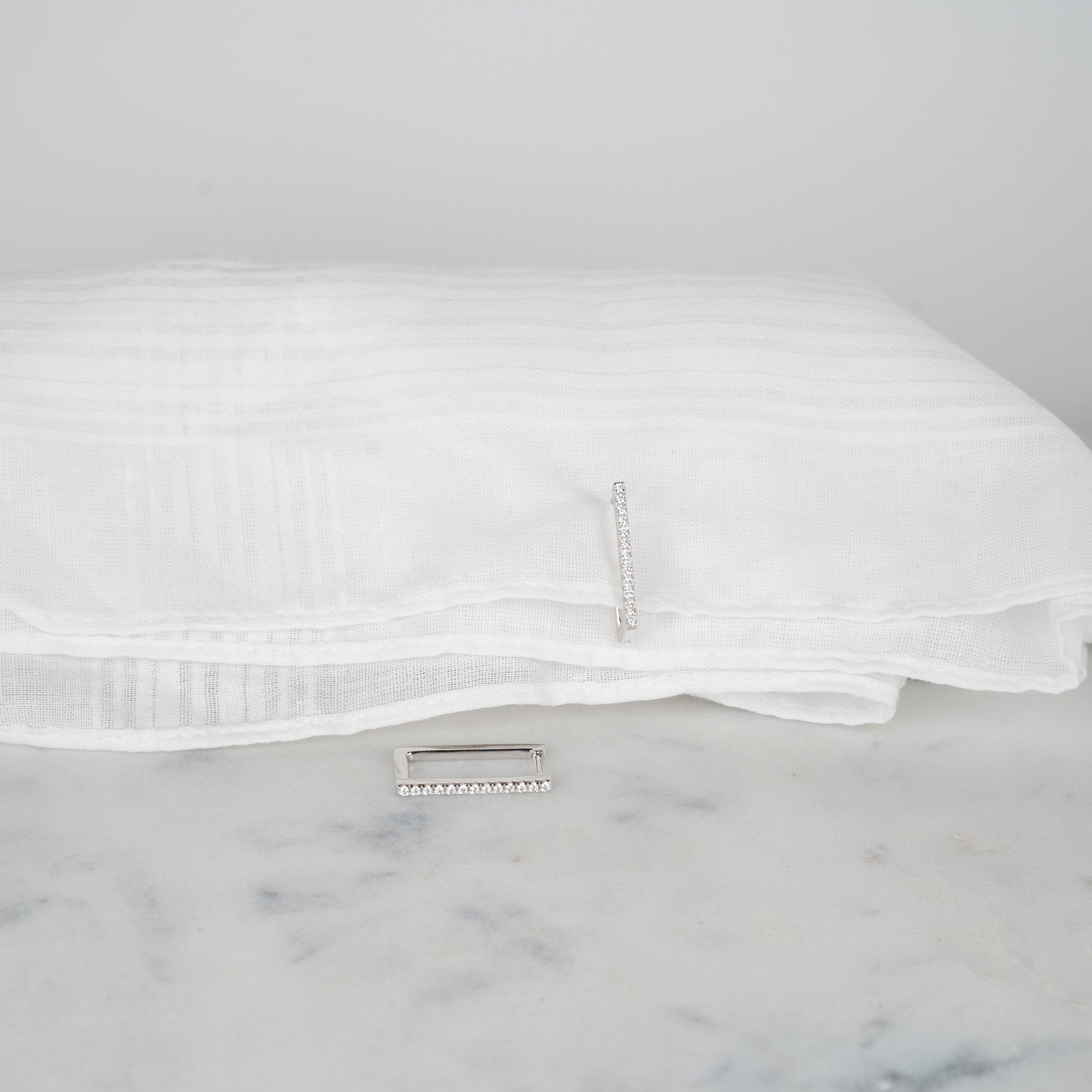 Boucles d'oreilles rectangulaires zirconium couleur argent posées sur un tissu blanc