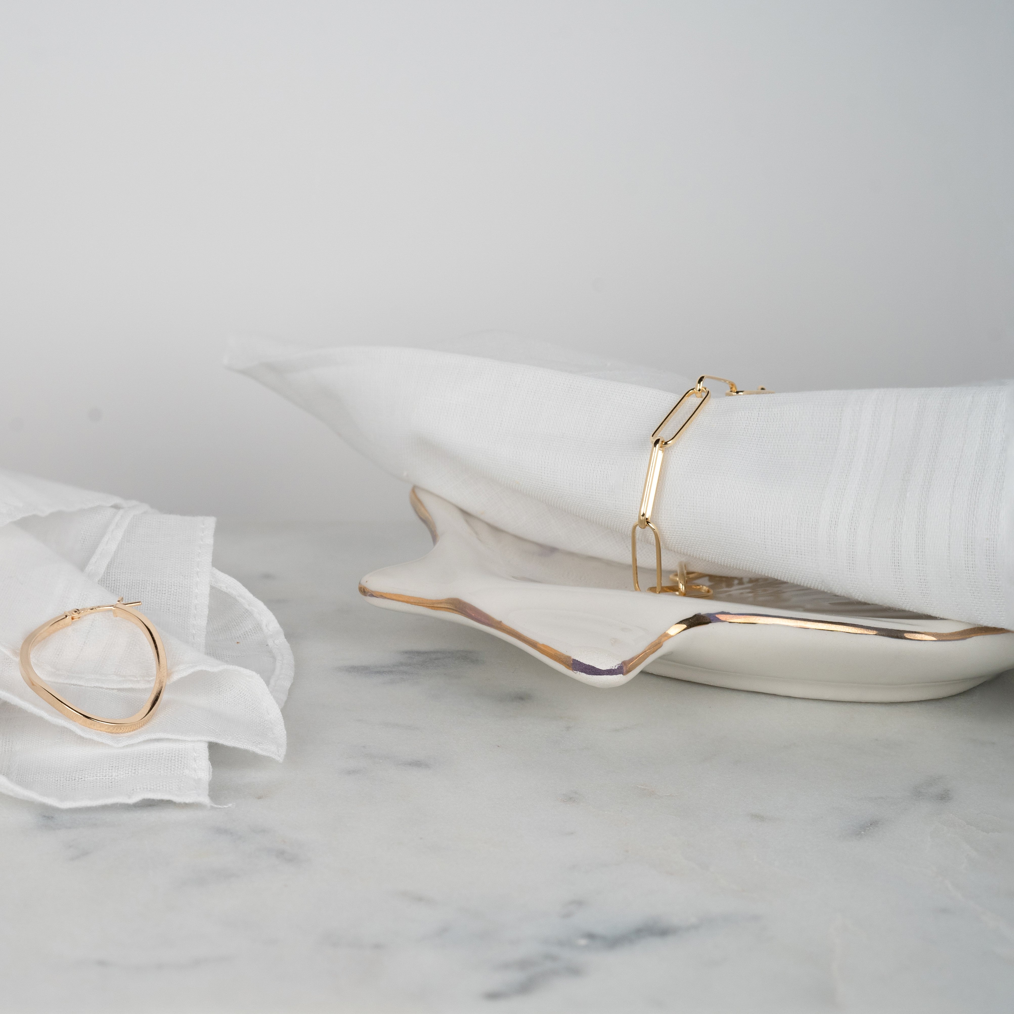 Bracelet maillon en argent couleur or jaune entourant un tissu blanc sur du marbre