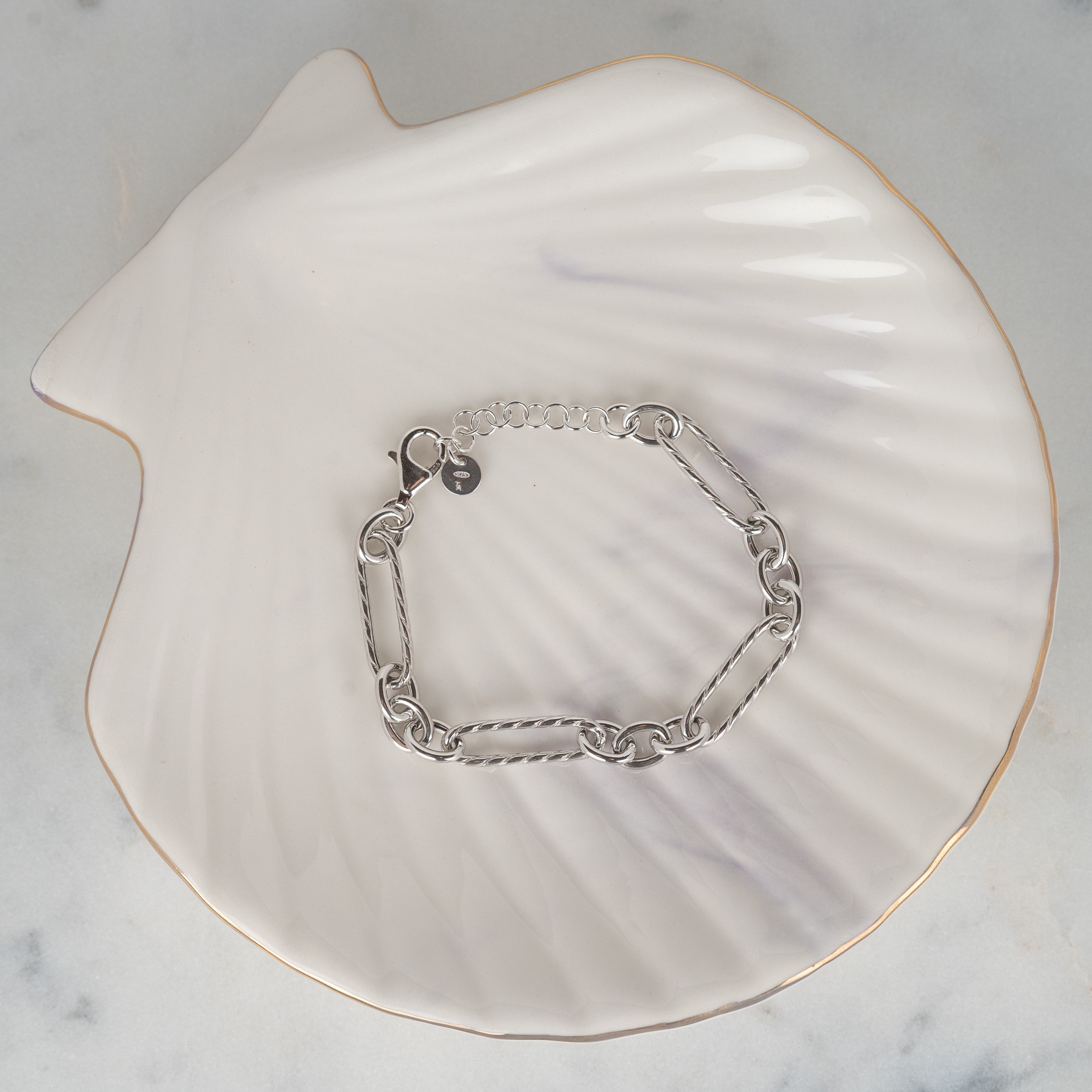 Bracelet maille marine en argent 925 rhodié posé sur un coquillage et du marbre