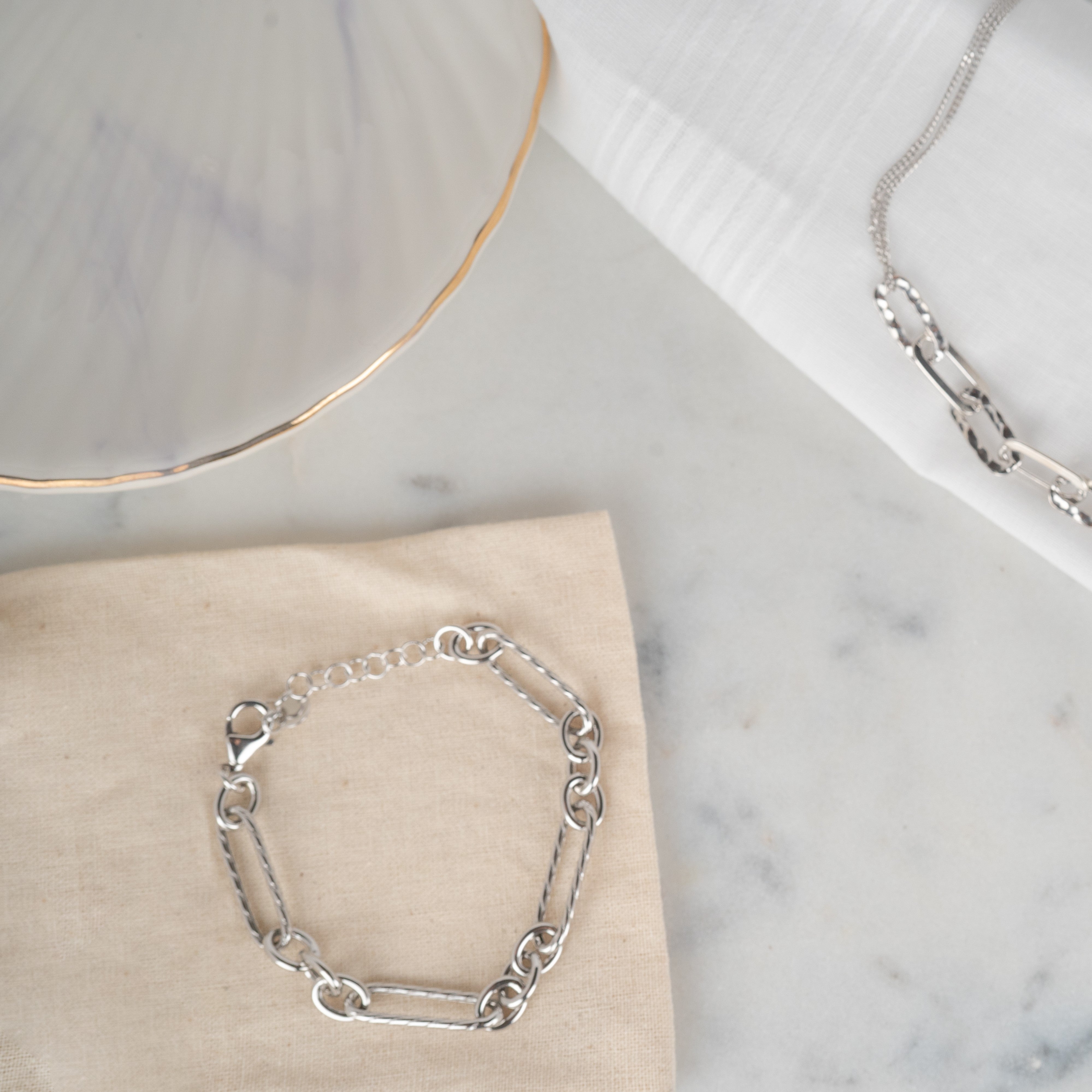 Bracelet maille marine en argent rhodié posé sur un tissu beige et du marbre