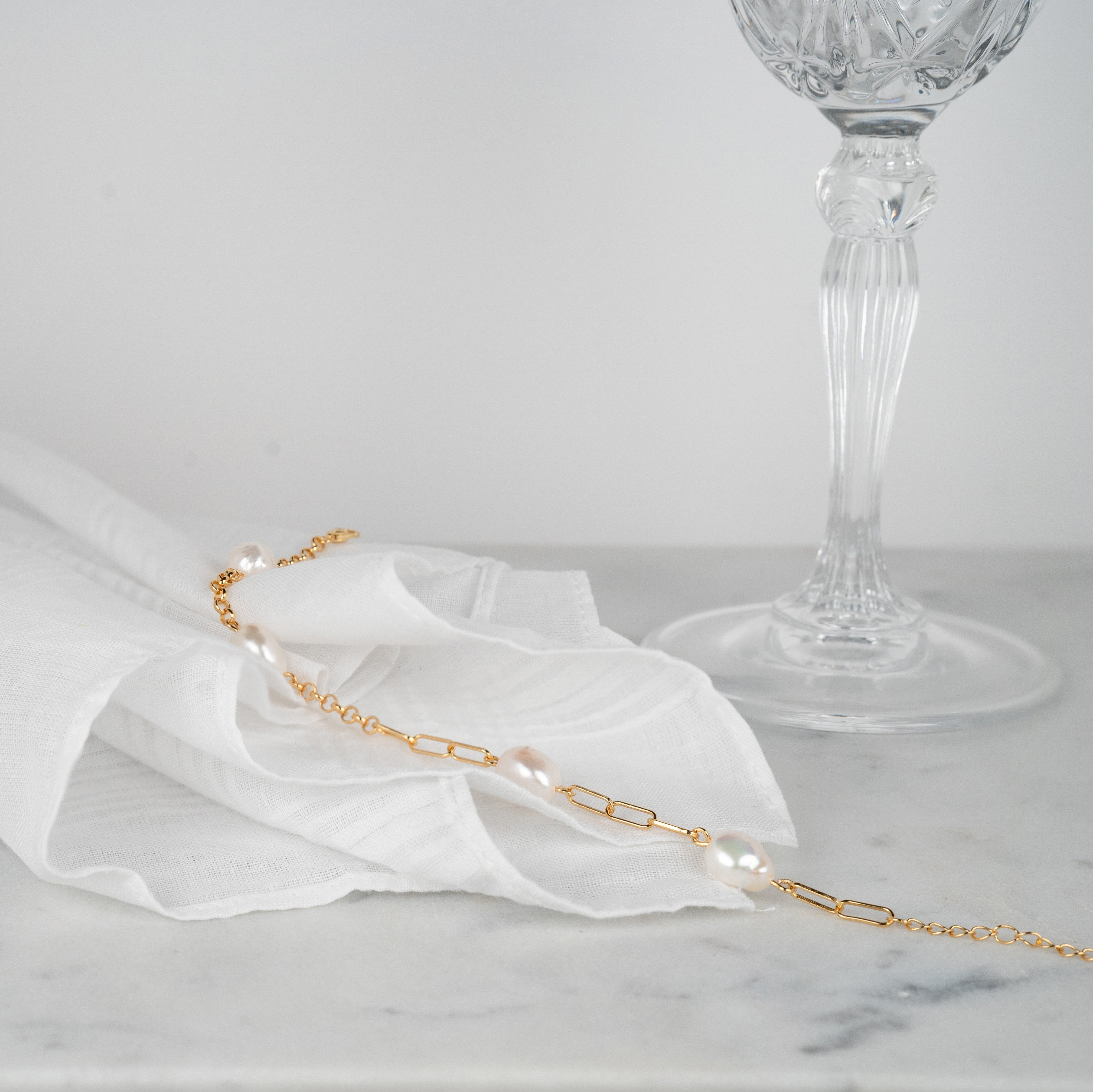 Zuchtperlenarmband aus gelbvergoldetem Silber mit Gliedern und Kette auf einem weißen Stoff gelegt