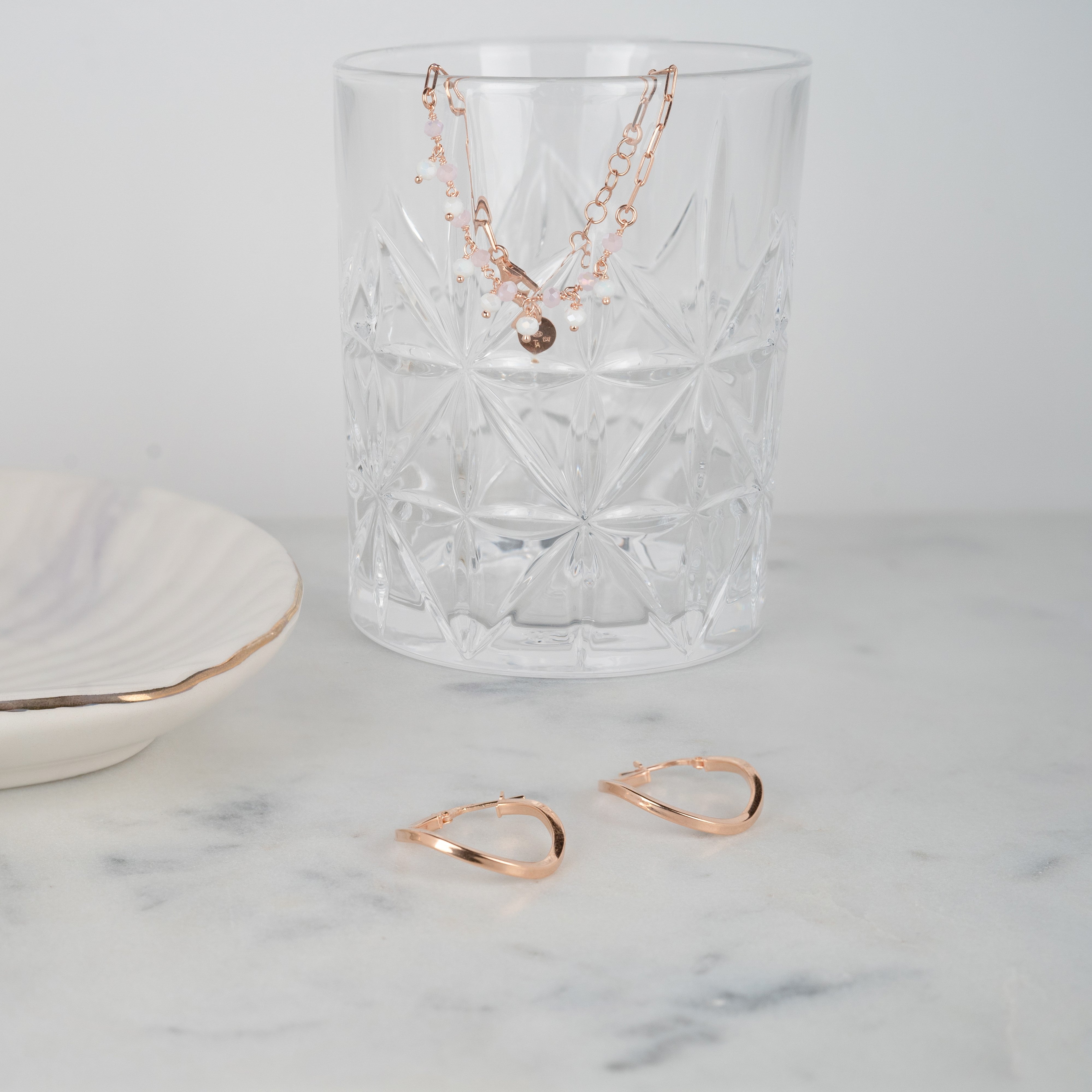 Armband aus rosa und weißem Quarz in roségoldfarbenem Silber, das auf einem Glas sitzt