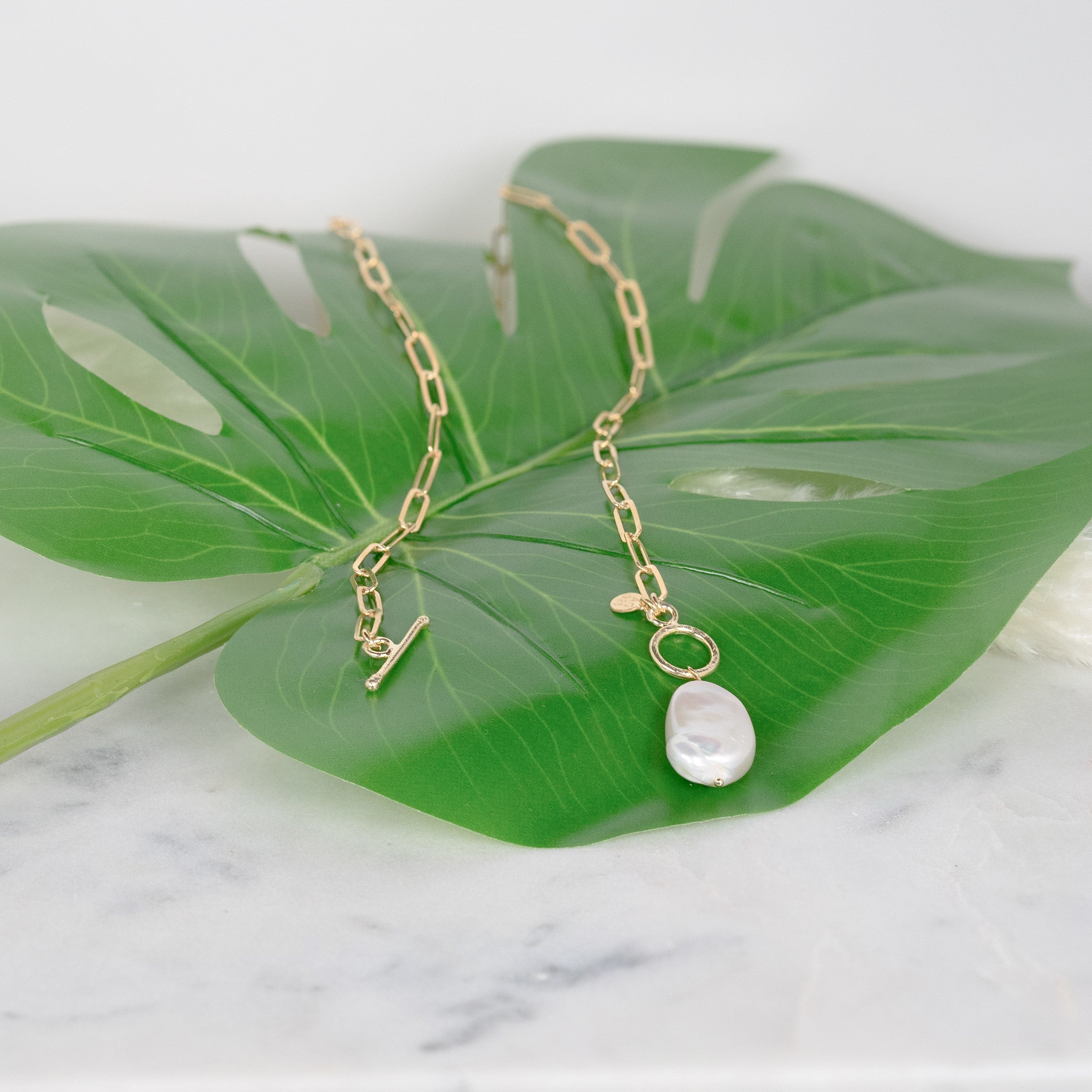 Zuchtperlenkette aus gelbvergoldetem Silber, die auf einem grünen Blatt sitzt