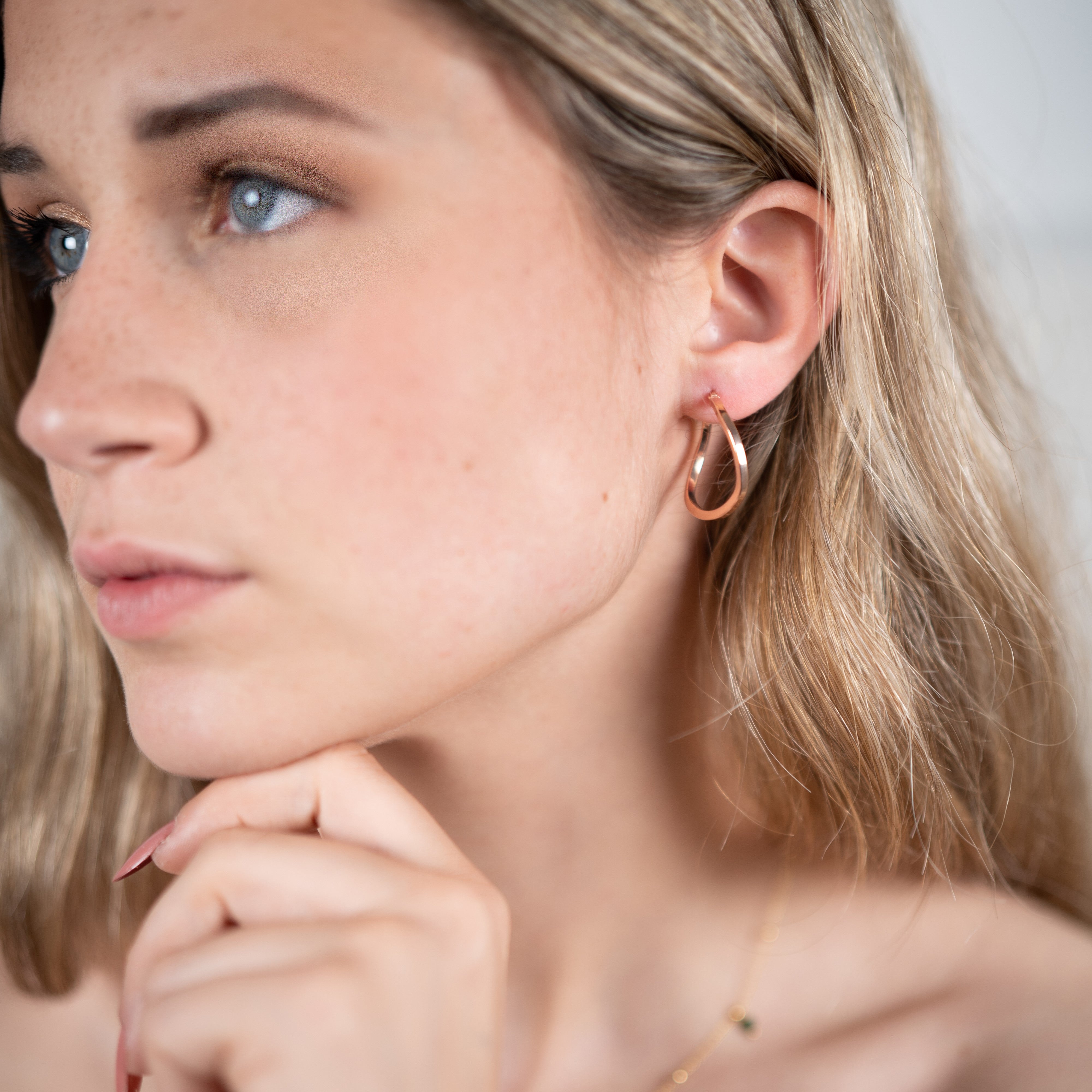 Boucles d'oreilles créoles asymétriques or rose portées sur un modèle