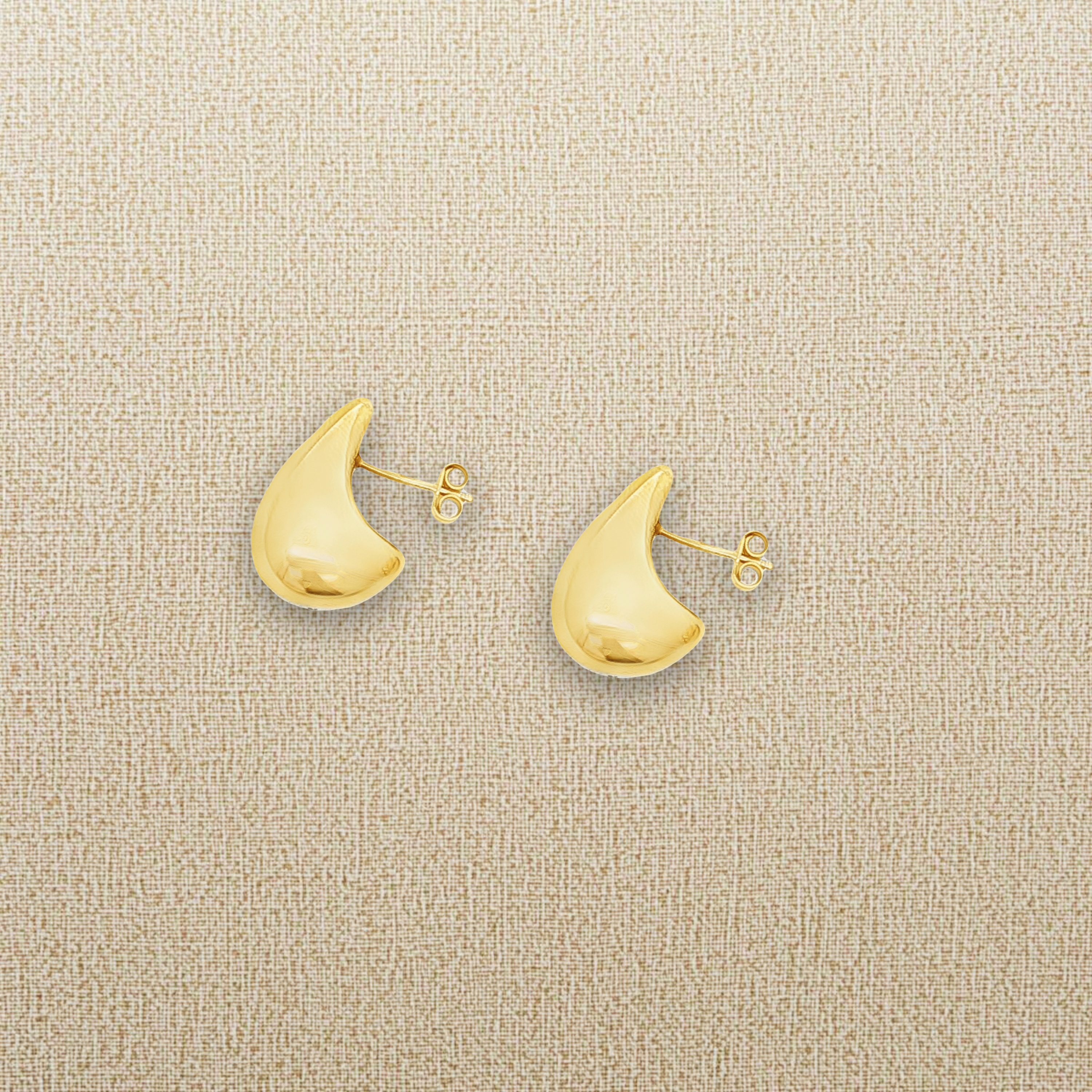 Boucles d'oreilles goutte posées sur un tissu beige