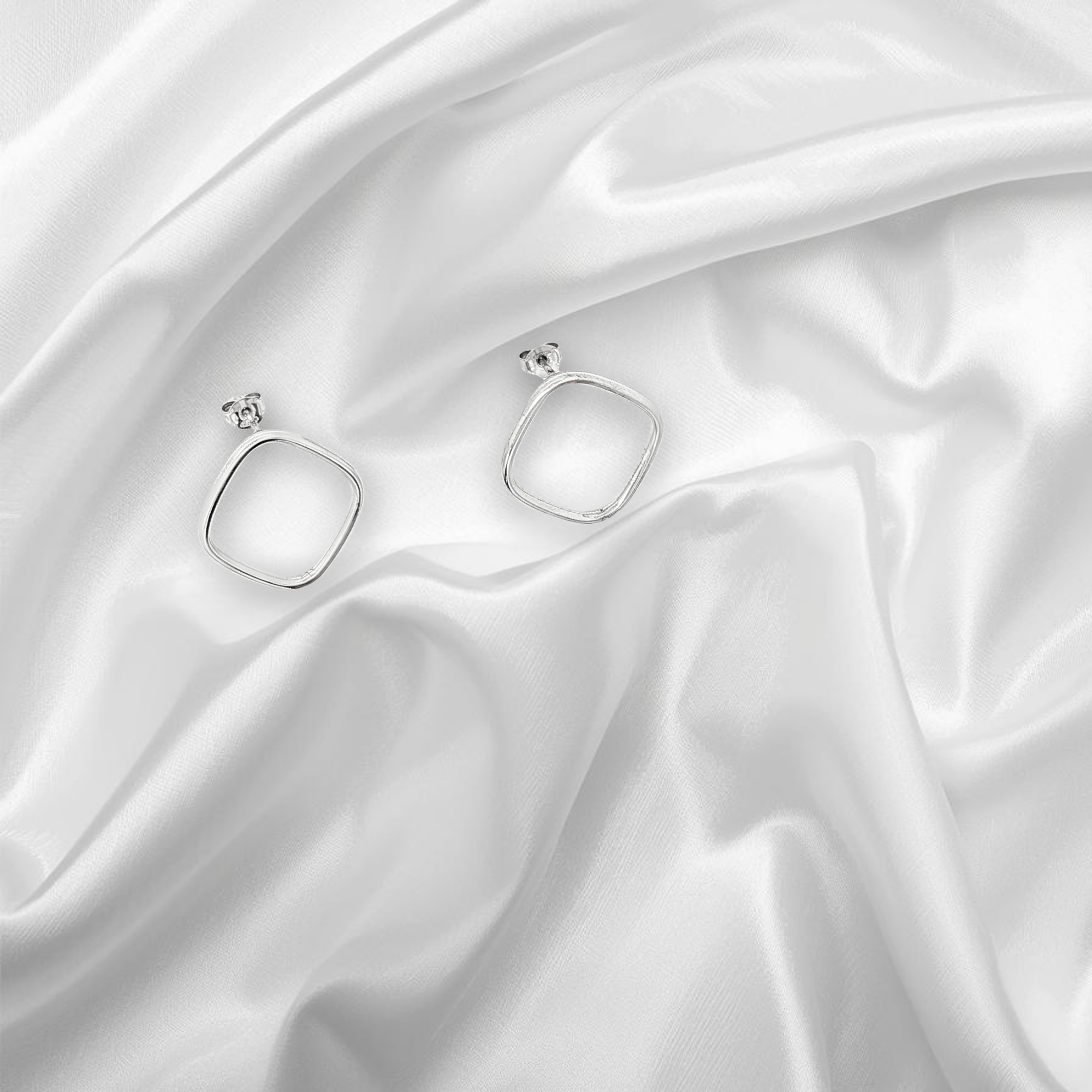 Boucles d'oreilles carrées en argent posées sur un tissu de soie blanc