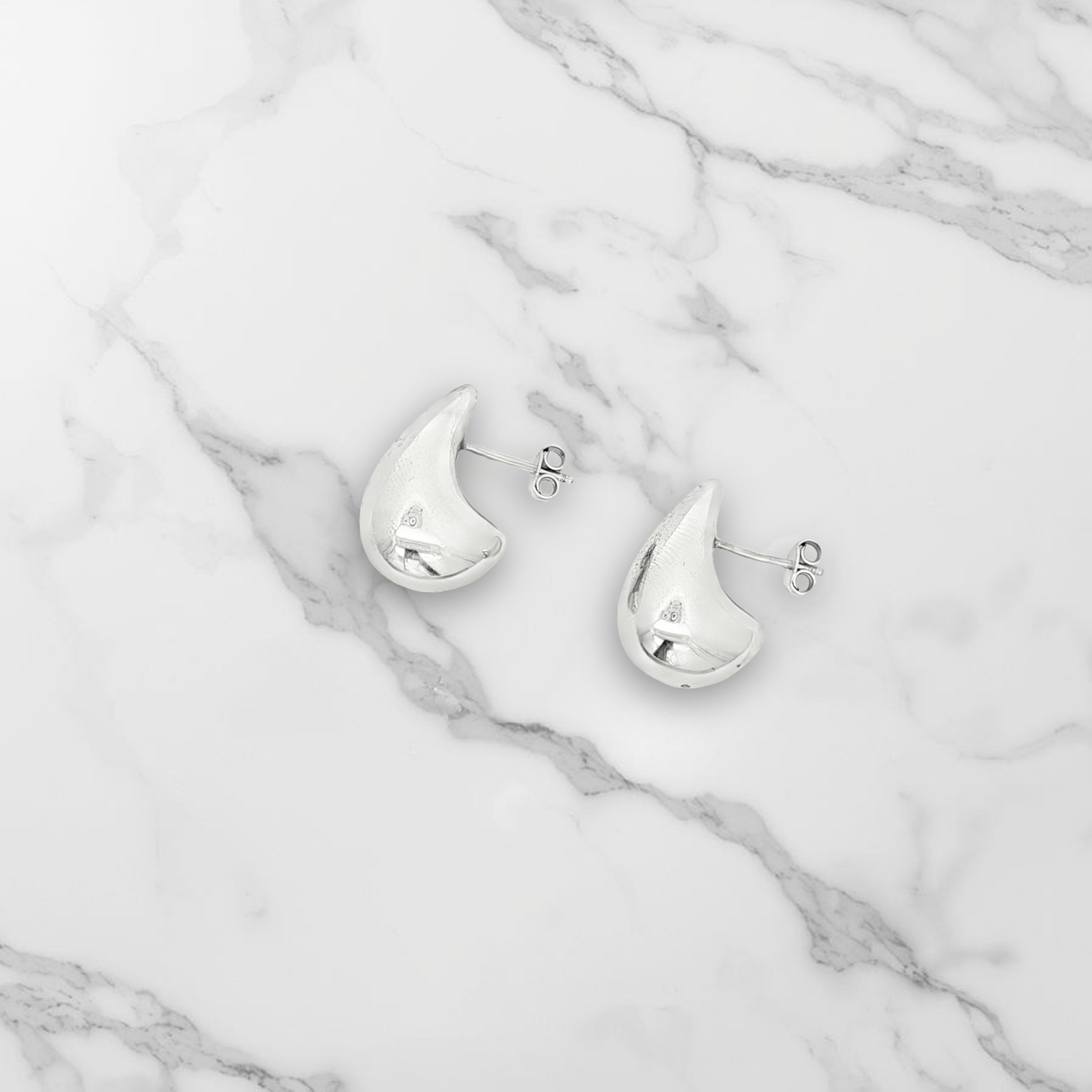 Boucles d'oreilles goutte en argent massif posées sur du marbre blanc