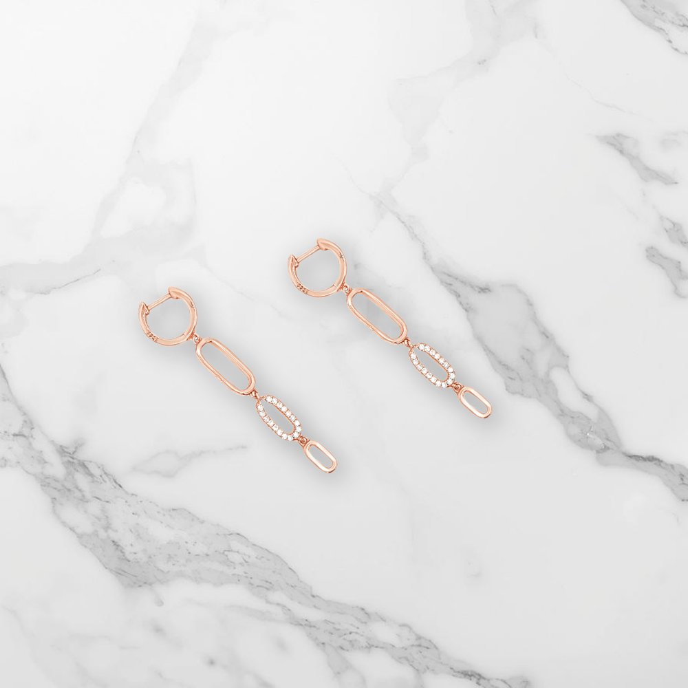 Boucles d'oreilles pendantes or rose avec des zircons posées sur du marbre