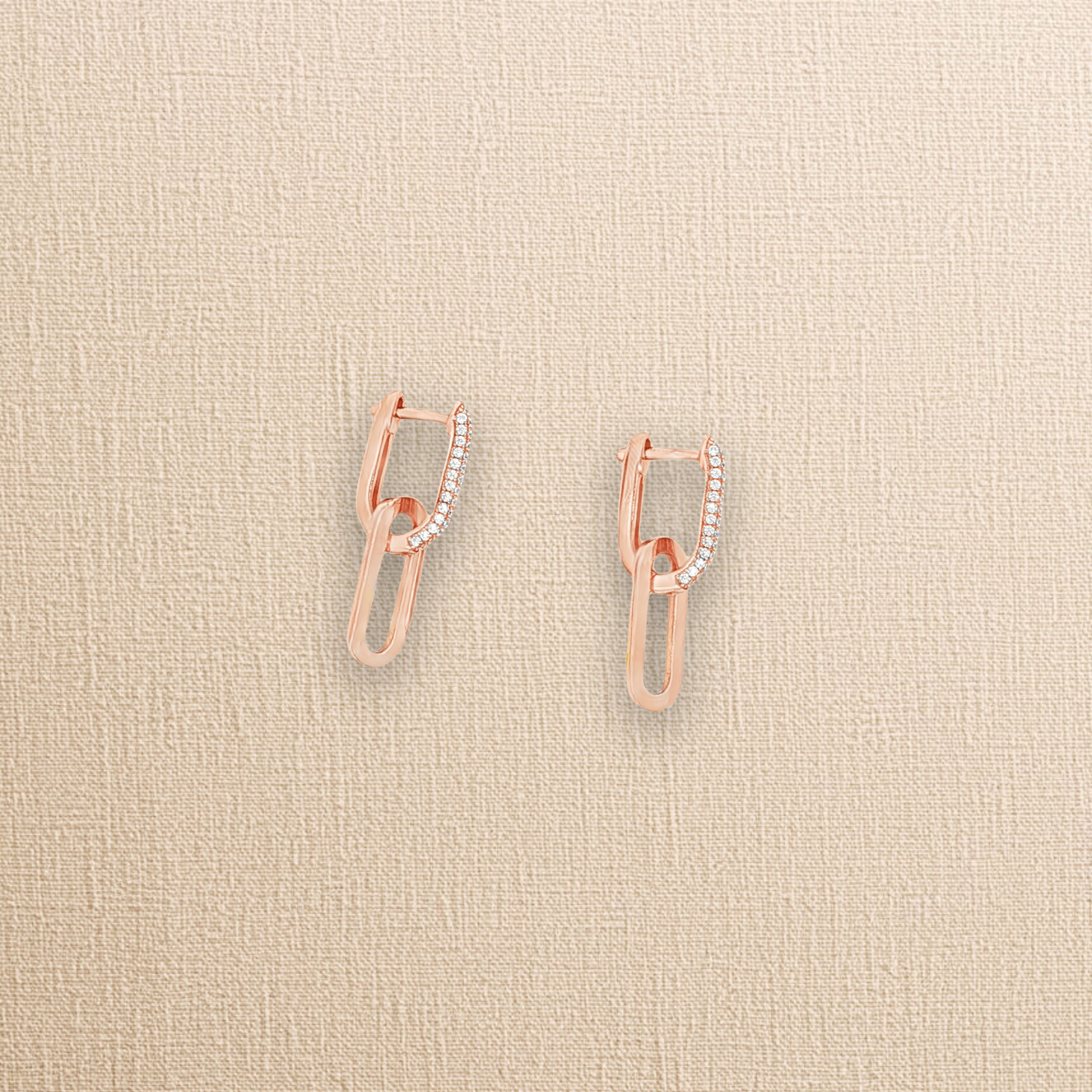 Boucles d'oreilles or rose et zircons posées sur un tissu beige