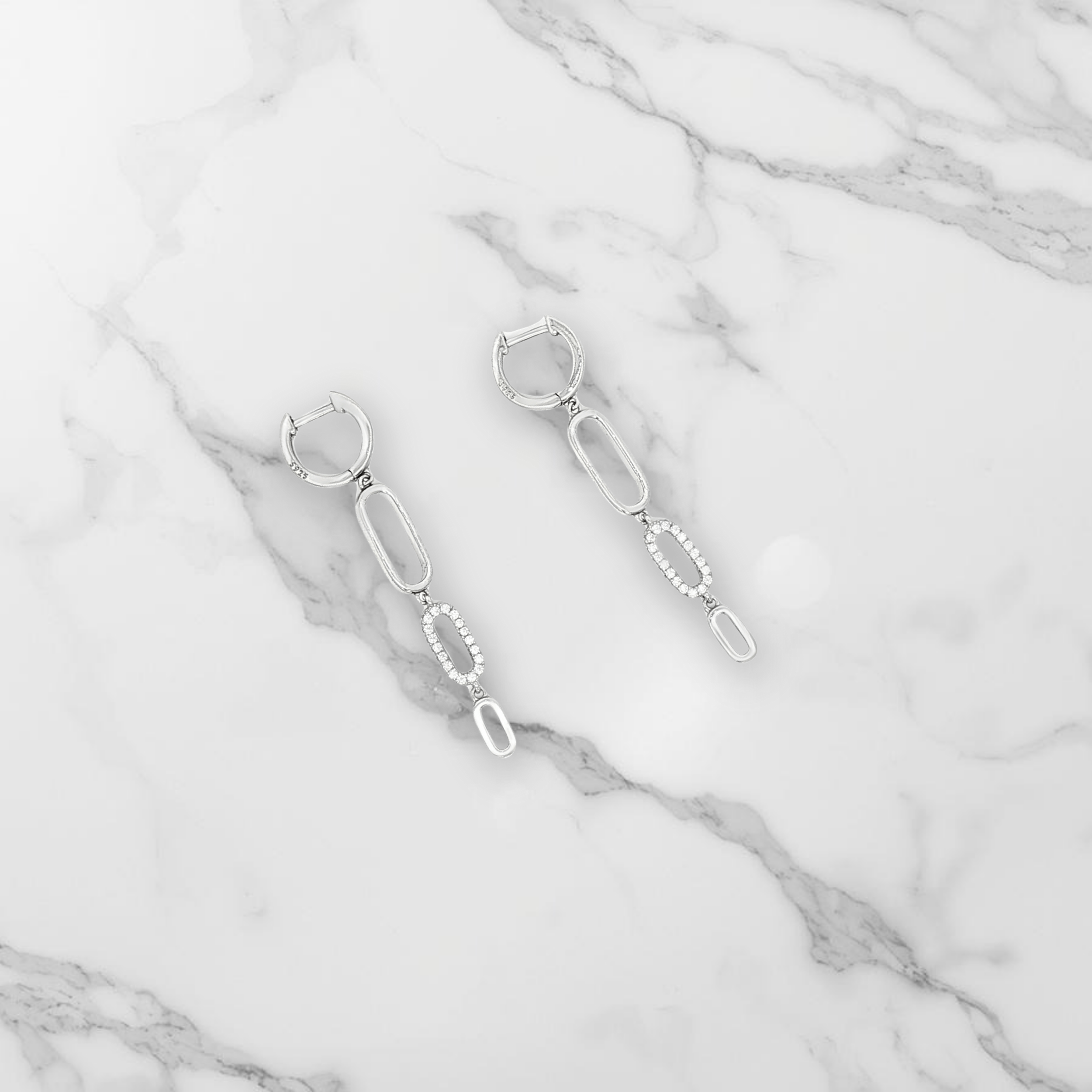 Un paire de boucle d'oreille pendante argent et zirconiums posée sur du marbre