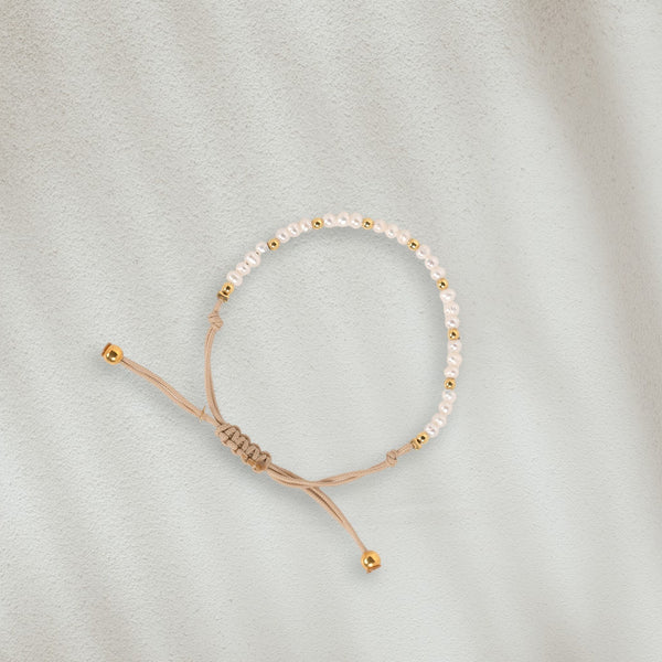 Bracelet en coton beige avec des perles naturelles posé sur du sable