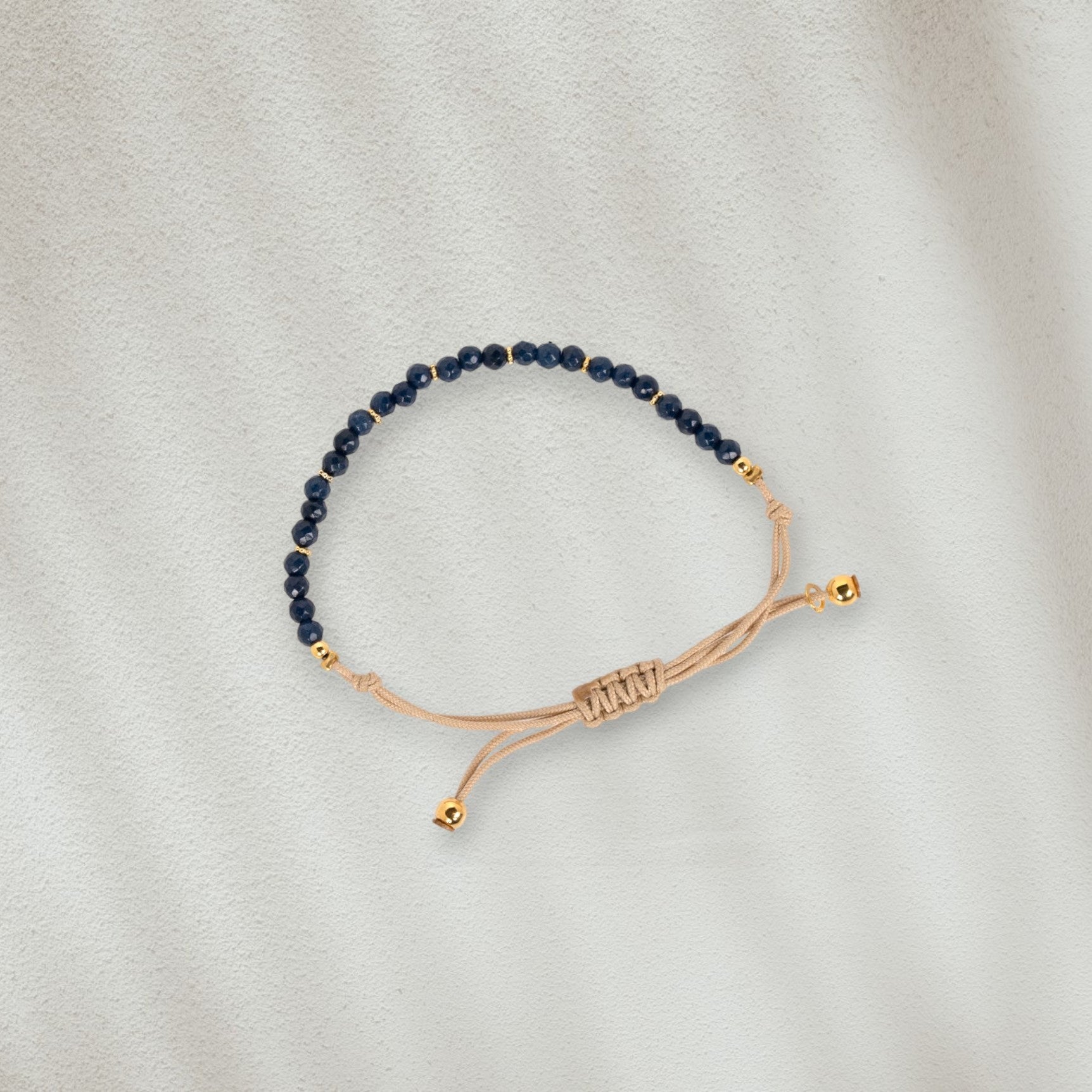 Bracelet en coton beige avec des pierres bleues marines posé sur du sable