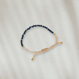 Bracelet en coton beige avec des pierres bleues marines posé sur du sable