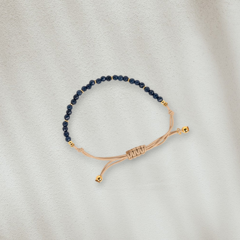 Bracelet en coton beige avec des pierres bleues marines posé sur du sable