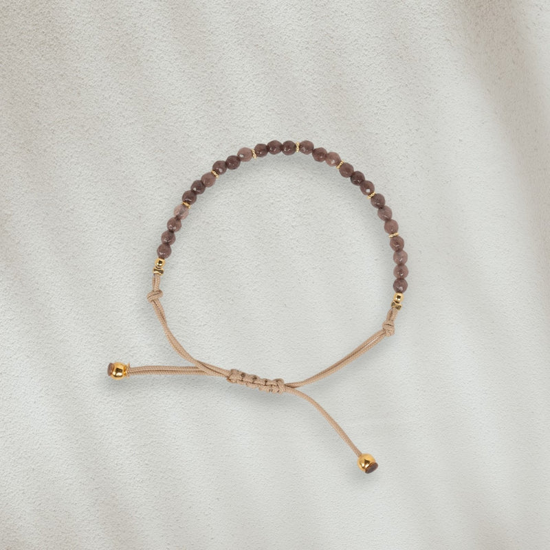 Bracelet en coton beige avec des pierres brunes posé sur du sable