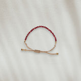 Bracelet en coton beige avec des pierres rouges posé sur du sable