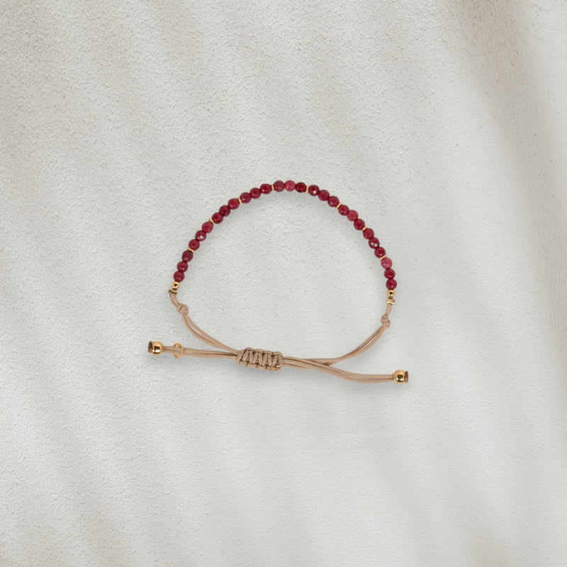 Bracelet en coton beige avec des pierres rouges posé sur du sable
