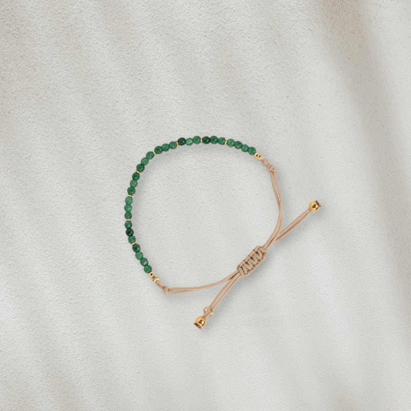 Bracelet en coton beige avec des pierres vertes posé sur du sable