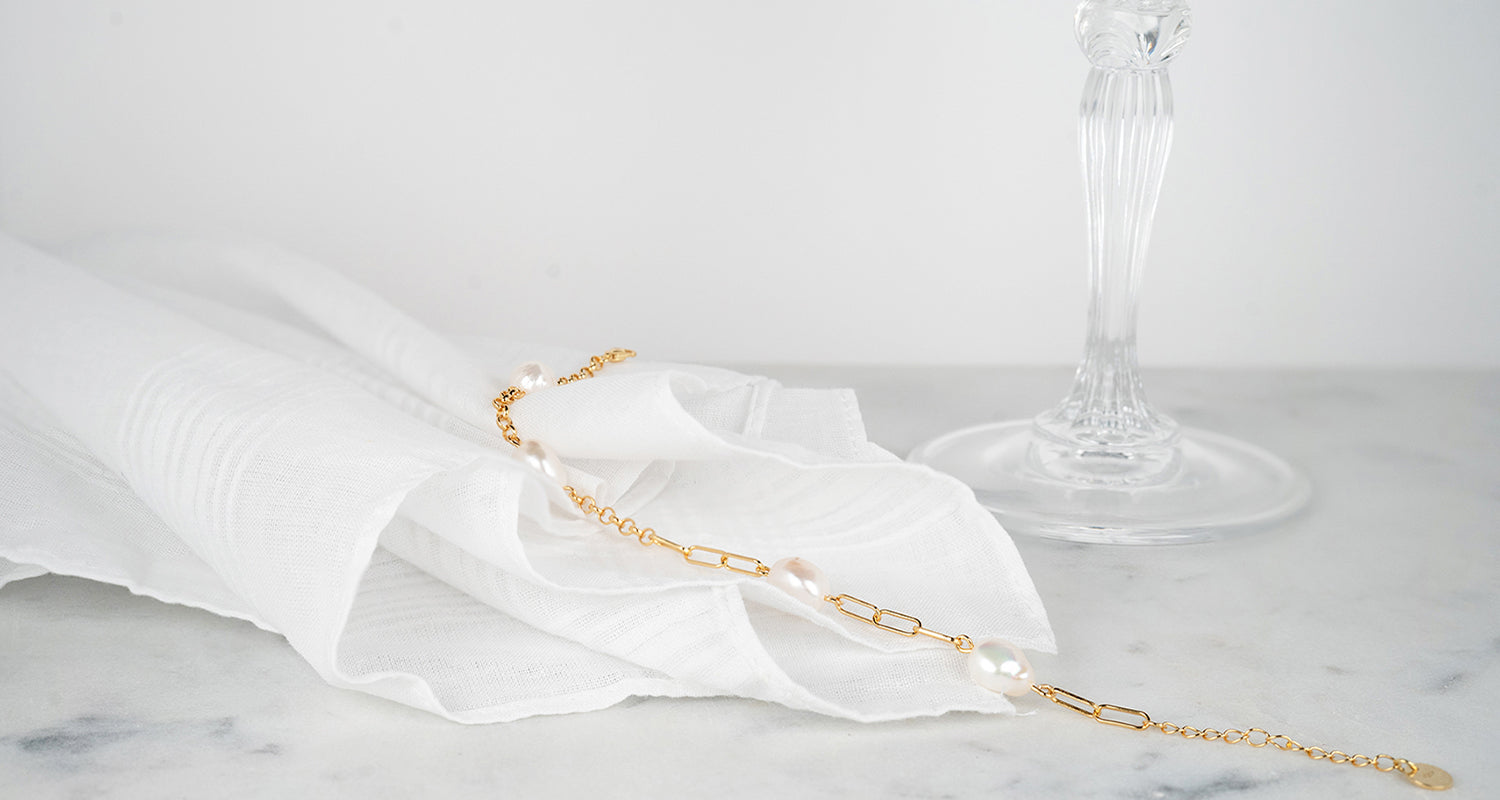 Bracelet chaîne de couleur or jaune avec des perles posé sur un tissu blanc
