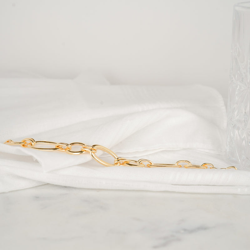 Bracelet gros maillons de couleur or jaune posé sur un tissu blanc
